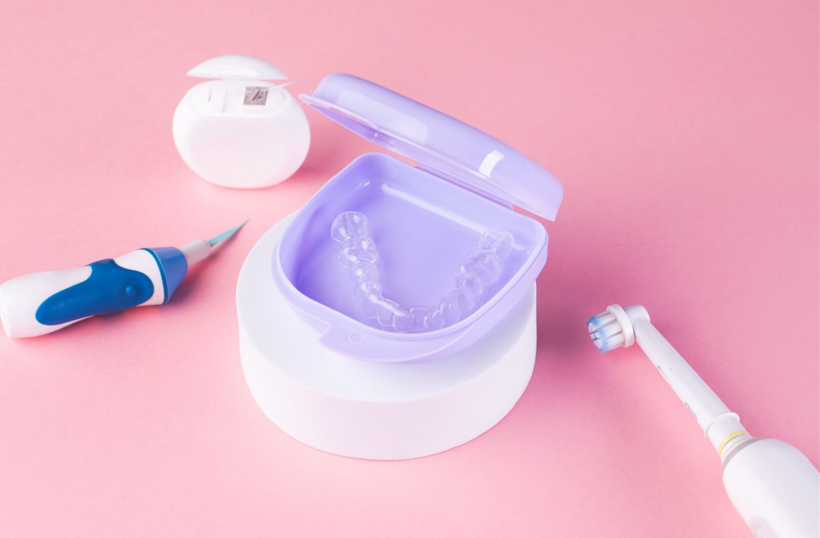 Clean Invisalign trays rest in their case, surrounded by cleaning tools for oral health.