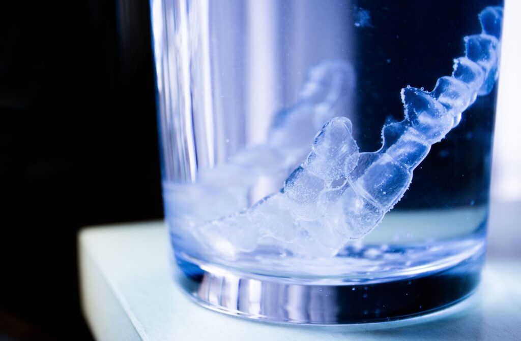 Invisalign trays soaking in a glass with lukewarm water and cleaning tablets.