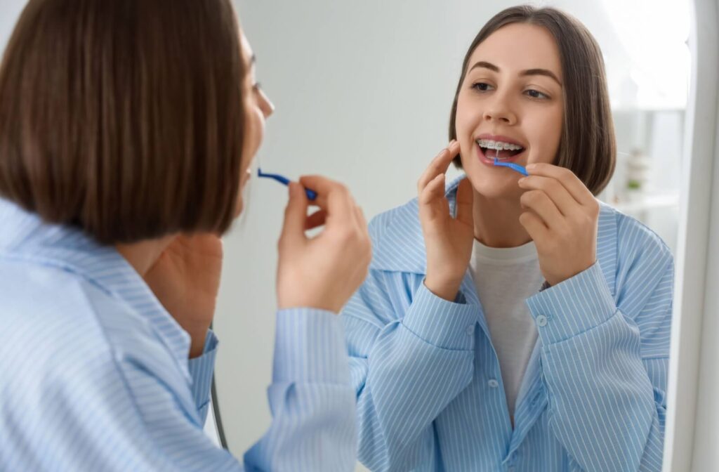 Young patient with braces using a flossing tool while looking in the mirror.