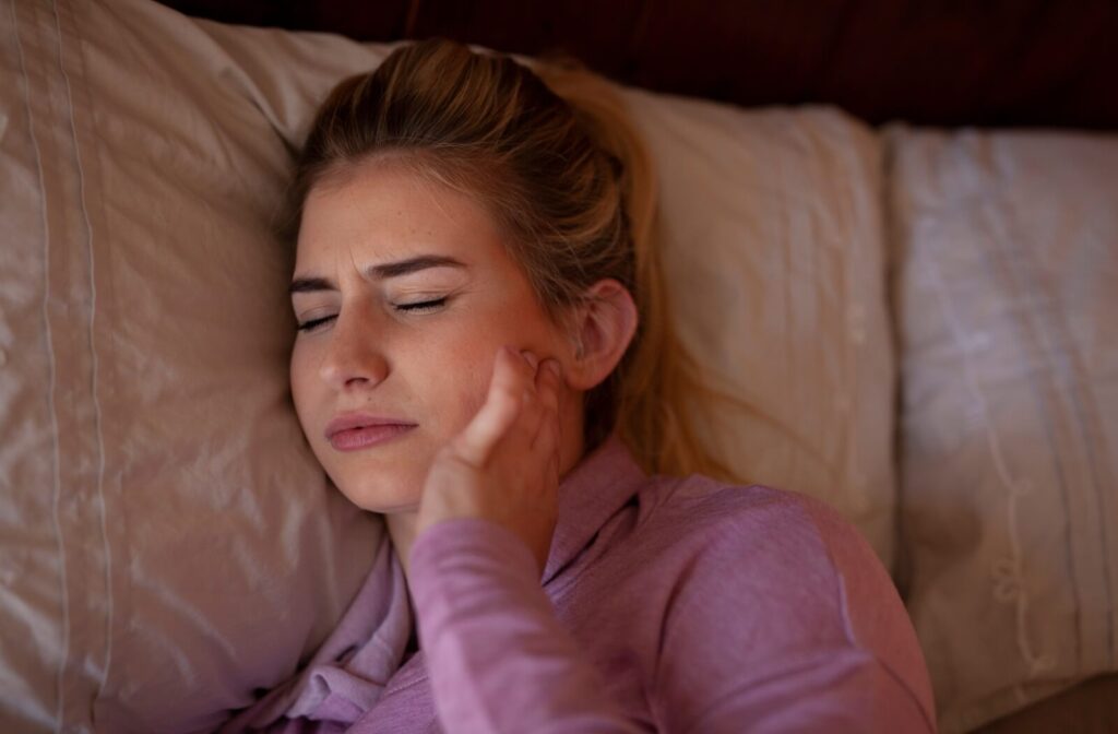 Person lying against a pillow and holding the side of their face in discomfort.
