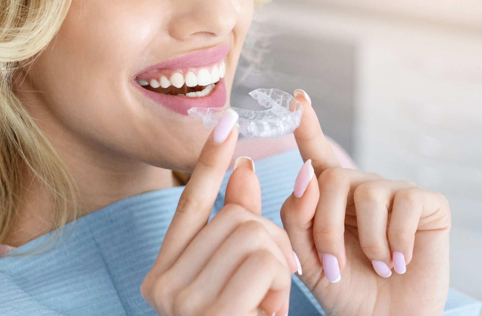 Person holding a clear Invisalign aligner near their smile.