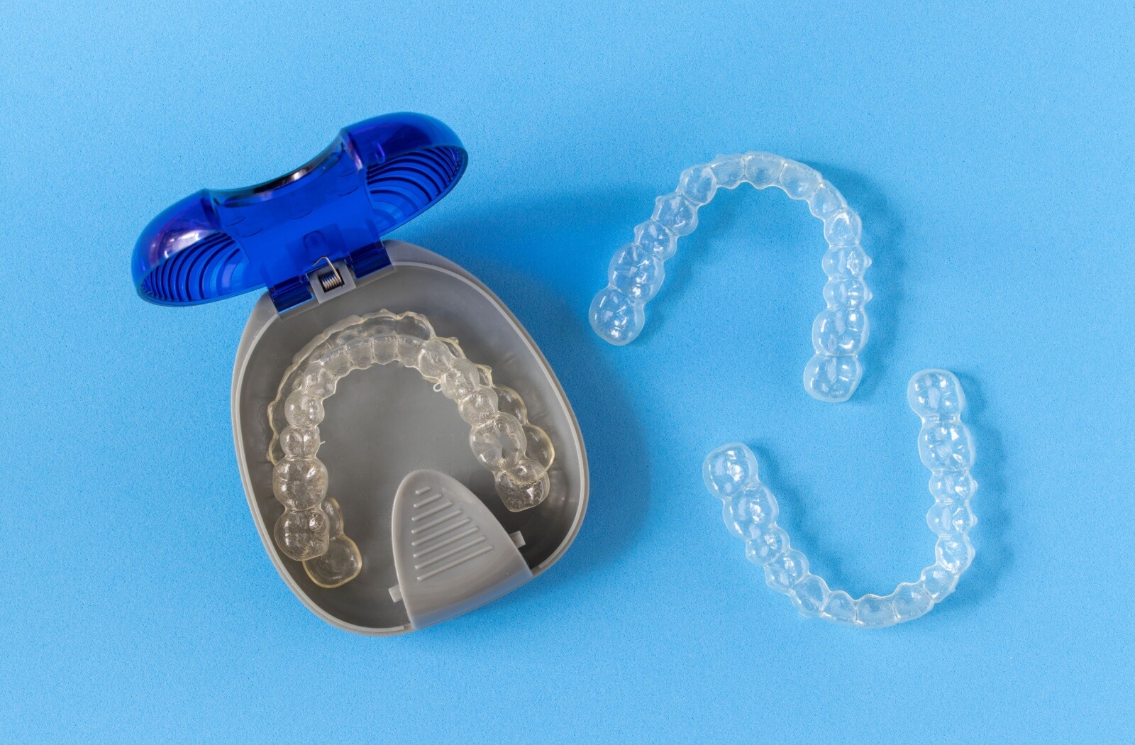 Clear dental retainers next to an open storage case.