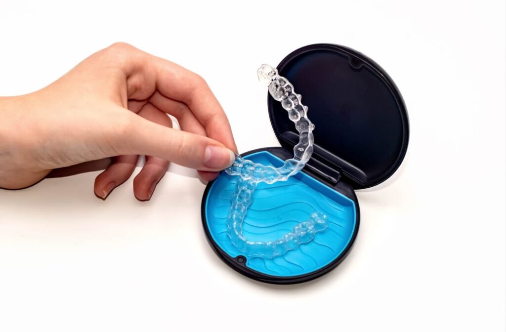 A hand placing a clear plastic aligner into a black and blue protective storage case, demonstrating proper care during Invisalign treatment.